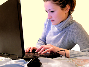 Woman typing on laptop on bed